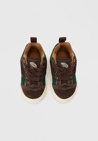 Pruunid ja rohelised nahkkingad valgete kummitaldadega, tikitud detailid ja kuldsetoonilised aukud. Omab tagumist tõmbeaasat mugavaks jalga panemiseks.