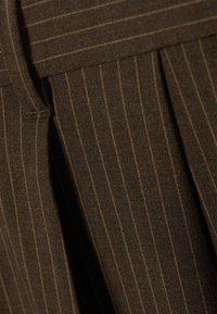 Tela marrón con finas rayas verticales en un tono más claro. El material tiene una textura suave con un diseño plisado.