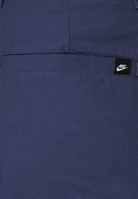 Pantalones cortos de tela azul marino con un acabado texturizado, que presentan una pequeña etiqueta del logo negro de Nike en el bolsillo trasero.