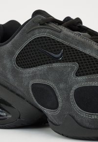 Baskets noires et grises avec des matériaux en daim texturé et en mesh, présentant un logo Nike brillant proéminent et des détails de design découpés distincts.