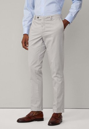 Pantalons en coton gris clair avec une coupe slim, devant plat, et une fermeture à un seul bouton, associés à des mocassins en cuir marron.
