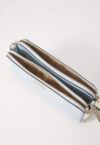 Světle modrá kožená crossbody taška se dvěma přihrádkami a zlatými zipy, s hnědým vzorovaným interiérem a stříbrným řetízkovým popruhem.