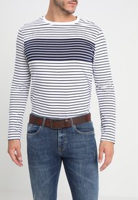 Langärmliges gestreiftes Hemd in Marineblau und Weiß mit Rundhalsausschnitt. Kombiniert mit blauen Jeans und einem braunen Gürtel für einen lässigen Look.