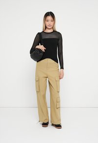 Musta pitkähihaisellinen paita, jossa on läpinäkyvä paneeli, ja beige cargo-housut, joissa on sivutaskut. Musta laukku ja platform-kengät täydentävät asua.