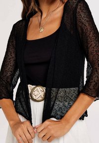Czarny, przejrzysty kardigan z rękawami o długości trzy czwarte. Tkanina o fakturze, otwarty przód, zestawiony z jasnym paskiem z ozdobną klamrą.