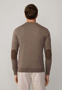 Brązowy sweter robiony na drutach z długimi rękawami, okrągłym dekoltem i kontrastowymi łaty na łokciach. Gładka tekstura i dopasowany krój. Wzmocnione mankiety i dół.