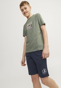 Grön bomull t-shirt med färggrafisk tryck och marinblå sweatshirtshorts med en vit logotyp på underbenet, båda i avslappnad passform.