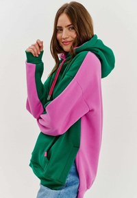 Mikina s kapucňou s dizajnom v zelenej a ružovej farbe, vyrobená z mäkkého materiálu, s veľkou prednou vreckom a kapucňou s šnúrkou.