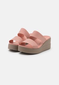 Paire de sandales compensées roses avec deux larges brides et semelles beiges sur fond blanc.