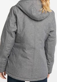 Grå, huva jacka med en texturerad yta, som har sömdetaljer och en logotyp patch på vänster axel. Inga synliga stängningar.