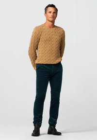 Gebreide beige trui met een gestructureerd kabelpatroon en een ronde hals, gecombineerd met donkergroene corduroybroek en zwarte enkellaarzen.