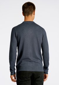 Mörkblå långärmad polo-sweater med en stickad struktur, med en krage och ribbade ärmslut, sedd bakifrån.