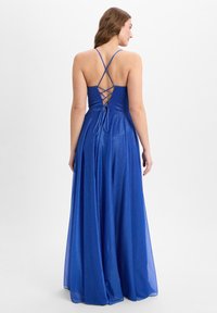 Langes blaues Kleid mit schimmerndem Finish, offener Rückseite und überkreuzten Trägern, sowie einem fließenden Rock, der elegant bis zum Boden fällt.