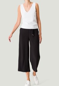 Witte mouwloze top met een V-hals, gecombineerd met zwarte, wijde broek met een koord in de taille. Draag het met witte sneakers.