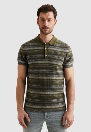 Mann trägt olivgrünes und graues gestreiftes Polohemd mit kurzen Ärmeln und hellblaue Jeans, steht vor schlichtem hellem Hintergrund.