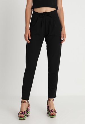 Personne portant un pantalon noir taille haute fuselé avec une ceinture à cordon et des talons compensés à plateforme ornés d'un motif zigzag coloré.