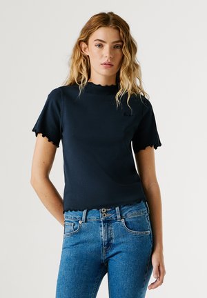 Marineblaues, geripptes T-Shirt mit kurzen, gerafften Ärmeln und einem gerafften Saum, hergestellt aus weichem Stoff. Kombiniert mit hoch taillierten blauen Jeans.