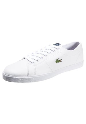 Biały niski sneaker z białymi sznurowadłami i zielonym logo krokodyla po boku, prezentowany na białym tle.