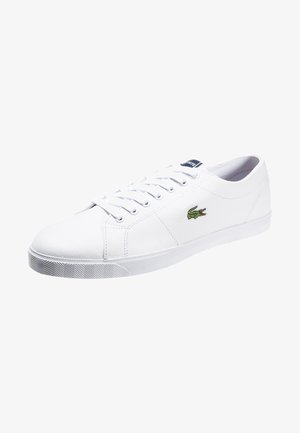 Biały niski sneaker z białymi sznurowadłami i zielonym logo krokodyla po boku, prezentowany na białym tle.
