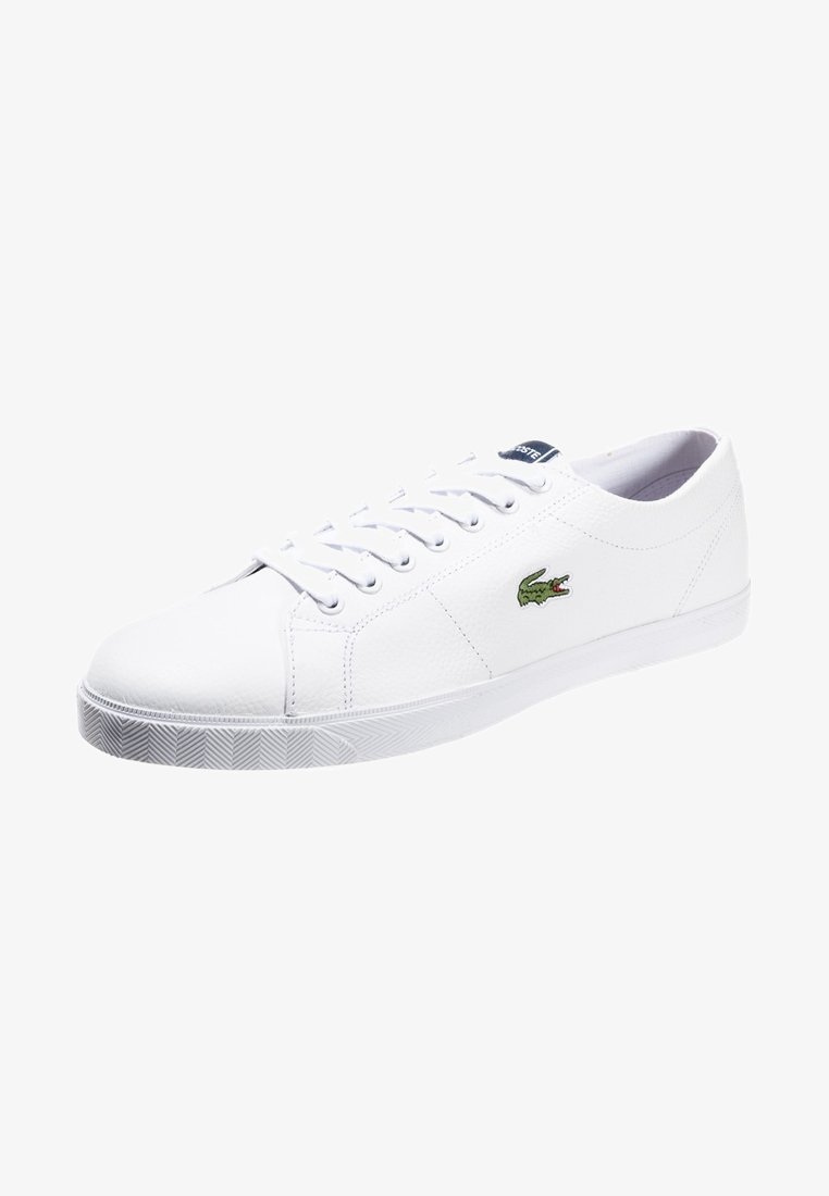 Baskets basses blanches avec lacets blancs et logo crocodile vert sur le côté, présentées sur fond blanc.
