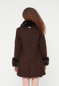 Καφέ  παλτό από μείγμα μάλλινης ύφανσης με ψεύτικο γούνινο γιακά και μανσέτες, με ευθεία γραμμή και μινιμαλιστικό σχεδιασμό, φορεμένο από πίσω όψη.