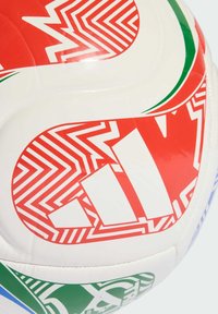 Tuvumā redzama balta futbola bumba ar sarkaniem, zaļiem un ziliem ģeometriskiem rakstiem un uz tās virsmas uzrakstītu treknu sarkanu tekstu.