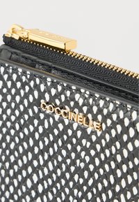 Fekete bőr pénztárca fehér gyémántmintával, arany cipzár hardverrel és dombornyomott "Coccinelle" márkanévvel az elején.