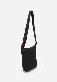 Černá kanvasová crossbody taška s obdélníkovým tvarem, nastavitelným popruhem, zipovým uzávěrem a malou značkovou etiketou na boku.