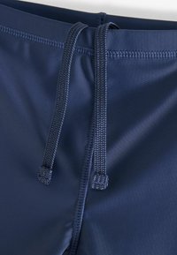 Mörkblå badshorts med en slät yta, utrustad med snörning i midjan och förstärkta sömmar för hållbarhet.