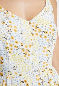 Blommig bomullsklänning med vit botten och blommor i gult, blått och brunt. V-ringning med knappar framtill och rynkad kjol.