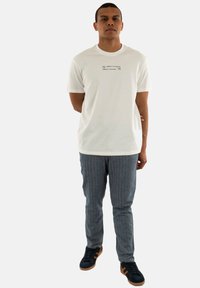 T-shirt en coton blanc avec col rond et texte imprimé ; assorti à un pantalon à rayures grises et des baskets noires avec des accents marron.