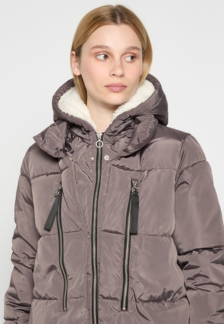 Puffige, mit Kapuze versehene Jacke in Grau mit einem weichen weißen Fleecefutter. Verfügt über Reißverschlusstaschen und eine gesteppten Textur. Verstellbare Kapuze mit Kordelzug.