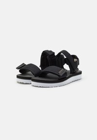 Sandalias negras con correas ajustables y una plantilla estampada. Suela blanca con textura antideslizante. Presenta un logo en la correa.