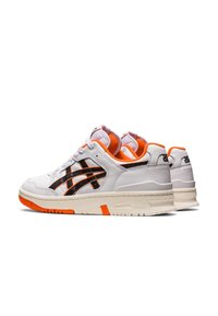 Baskets blanches avec des rayures noires, des accents orange et des semelles en caoutchouc texturées. Dotées d'une languette et d'un col rembourrés pour le confort.