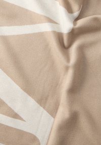 Material textil bej moale, cu o textură subtilă, cu un model abstract alb mare. Materialul pare ușor și neted.