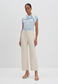 Lichtblauw T-shirt met korte mouwen en een sjaaldetail, gecombineerd met beige wijde broekspijpen en open teen sandalen, met een strakke, gladde textuur.