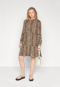 Abito leopardato con maniche lunghe, orlo a strati con volant e collo alto. Abbinato a sandali bianchi con cinturino e una piccola borsa beige.