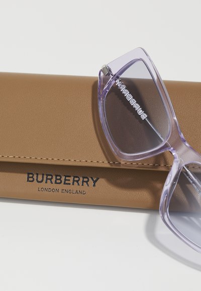 Violetti läpinäkyvät aurinkolasit lepäävät ruskeassa nahkakotelossa, jossa on musta "BURBERRY LONDON ENGLAND" -logo. Kotelolla on sileä pinta ja ommeltu yksityiskohta.