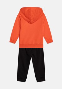 Sudadera naranja con capucha y pantalones de chándal negros. La tela es suave, con puños acanalados. El conjunto es informal y está diseñado para la comodidad.