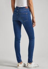 Jeans ajustados de mezclilla de color azul con una cintura alta. Presenta bolsillos traseros con un diseño cosido y una etiqueta de cuero marrón en la cintura.