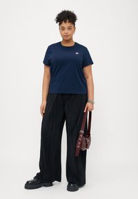 Mørkeblå bomulds T-shirt med korte ærmer og et lille logo, parret med sorte pliérede bukser med bred ben og en bordeaux håndtaske.