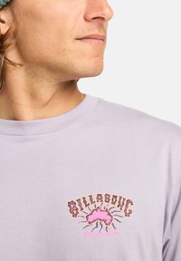 Világoslila, hosszú ujjú póló, amelyen egy színes grafika látható a "Billabong" és Ausztrália motívummal a mellrészen. Puha anyagból készült, kerek nyakkivágású.