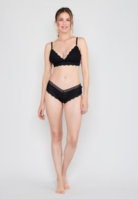 Czarny komplet bielizny koronkowej, który składa się z biustonosza z falbaniastymi krawędziami i pasujących majtek typu boyshort w poziome paski oraz wzory kwiatowe.