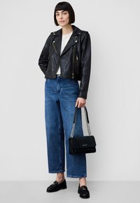 Svart bikerjacka i läder med guldfärgade detaljer, vit skjorta, högmidjade blå jeans i denim och svart mockaväska med kedjerem.