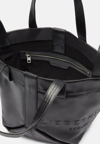 Czarna skórzana torba typu tote z solidnymi uchwytami, zapinaną na zamek wewnętrzną kieszenią oraz wytłoczonymi detalami marki na zewnątrz.