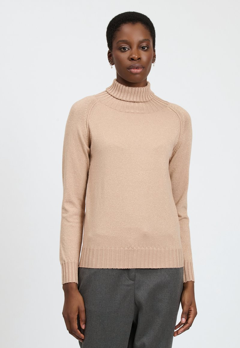 Maglione beige a collo alto con bordo e fondo a coste, tessuto liscio, design aderente e maniche lunghe, indossato sopra pantaloni grigi.
