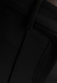 Nära bild av svart tyg med detaljerad sömnad och en vikt söm, som framhäver textur och skräddarsydd konstruktion.