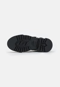 Suola di scarpa in gomma nera con scanalature profonde e righe pronunciate. Presenta un logo in rilievo e un motivo testurizzato per una migliore aderenza.