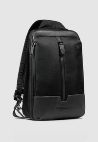 Zwarte rugzak met een bovenkant van gestructureerde stof, een glad leren onderkant, dubbele ritsen en een slank profiel, geschikt voor dagelijks gebruik of reizen.