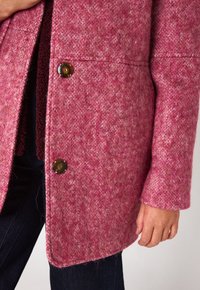 Cappotto rosa in misto lana con superficie texture, caratterizzato da un colletto a revers e chiusura con bottoni. Il tessuto presenta un motivo variegato.